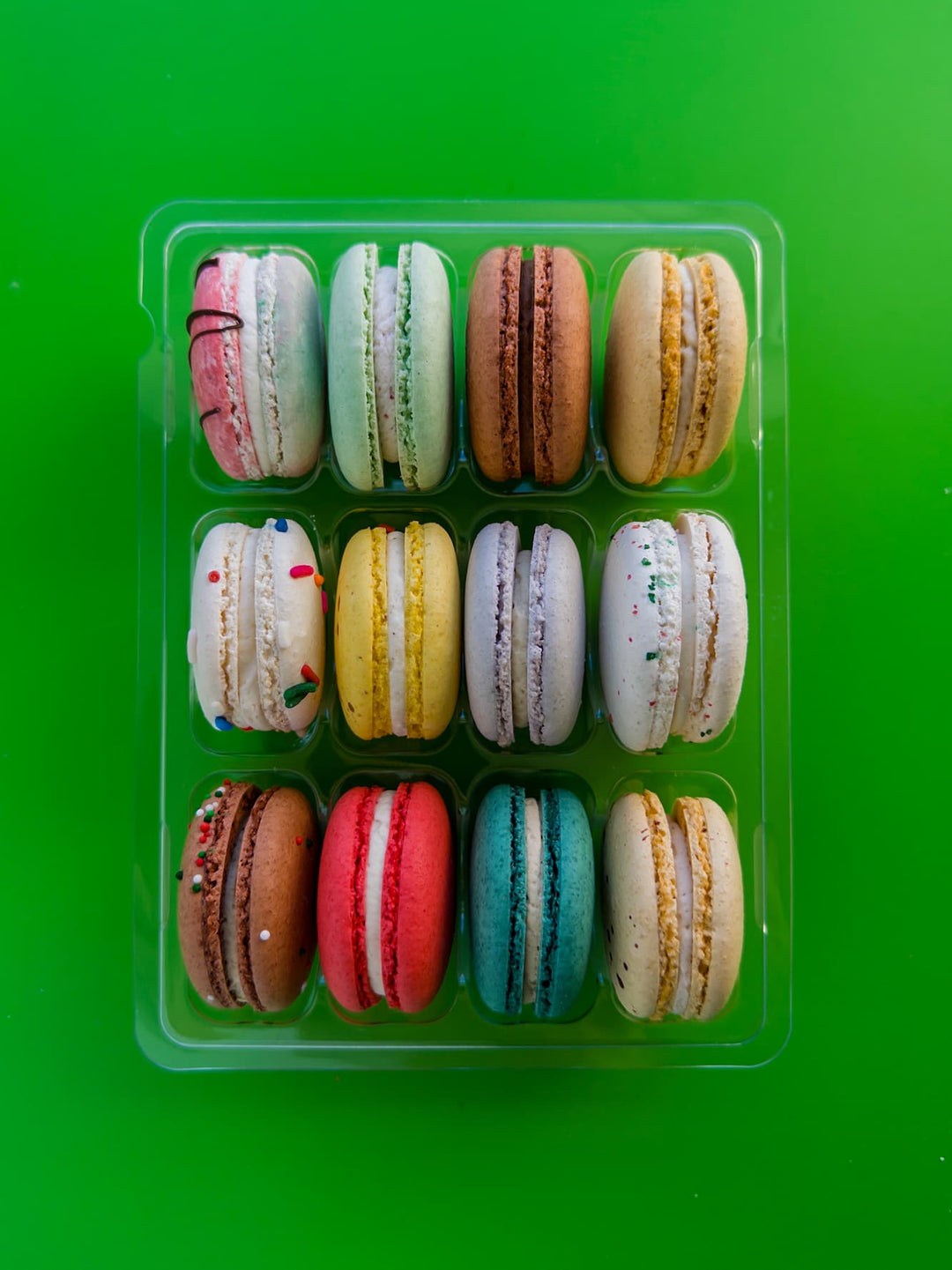 Assorted colorful macarons in a clear plastic container on a green background