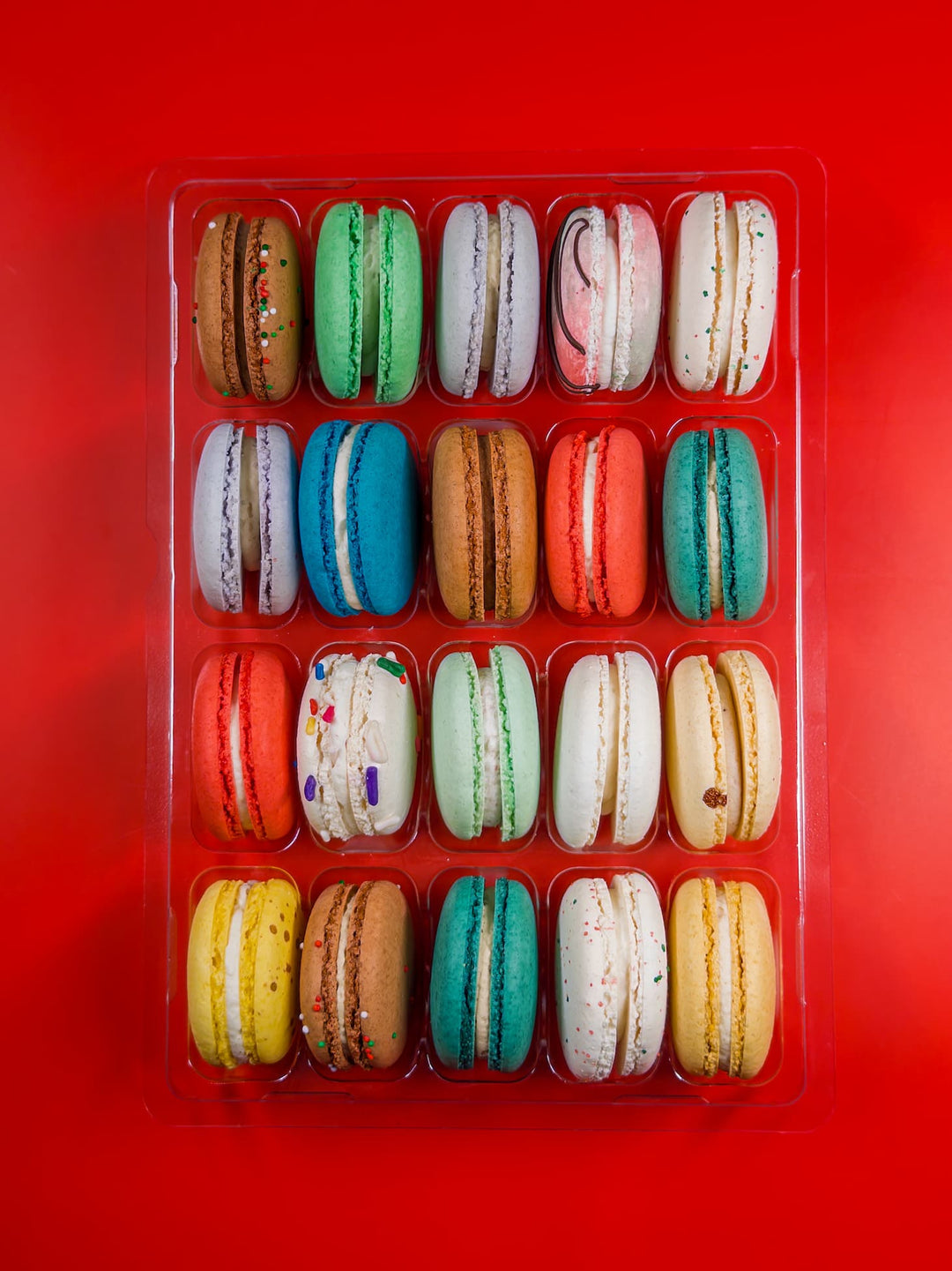 Assorted colorful macarons in a clear plastic container on a red background