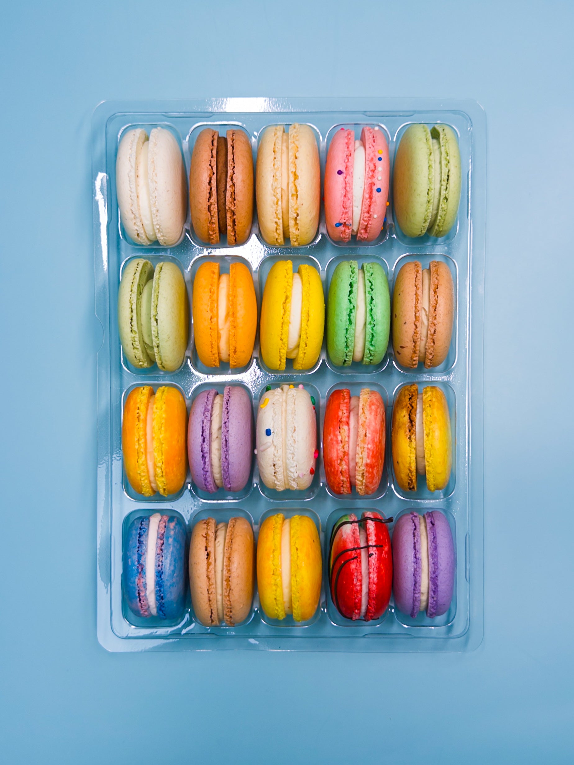 Assorted colorful macarons in a clear plastic container on a blue background