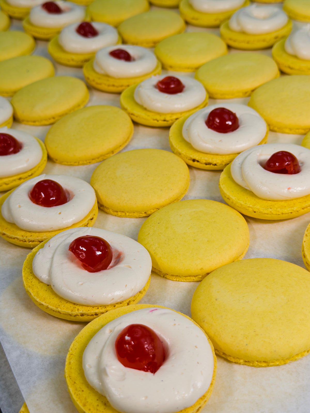 open face yellow macarons with a cherry middle surrounded by a white buttercream