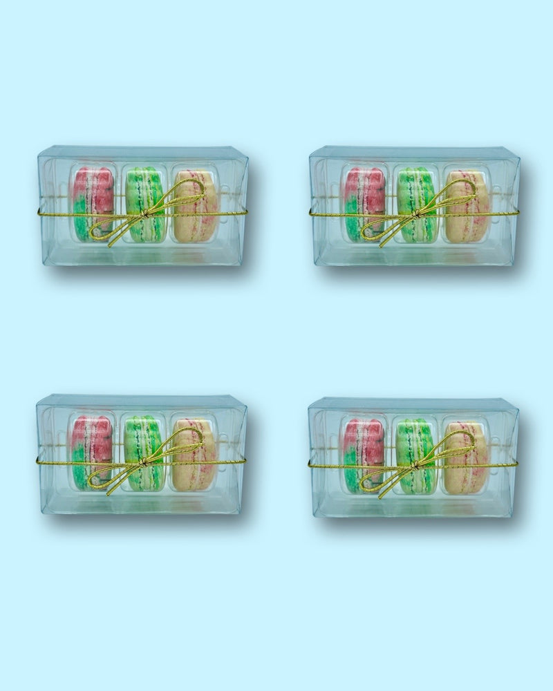 Three pack gift boxes of macarons with a gold bow on each, presented in a transparent packaging with visible colorful macarons inside.