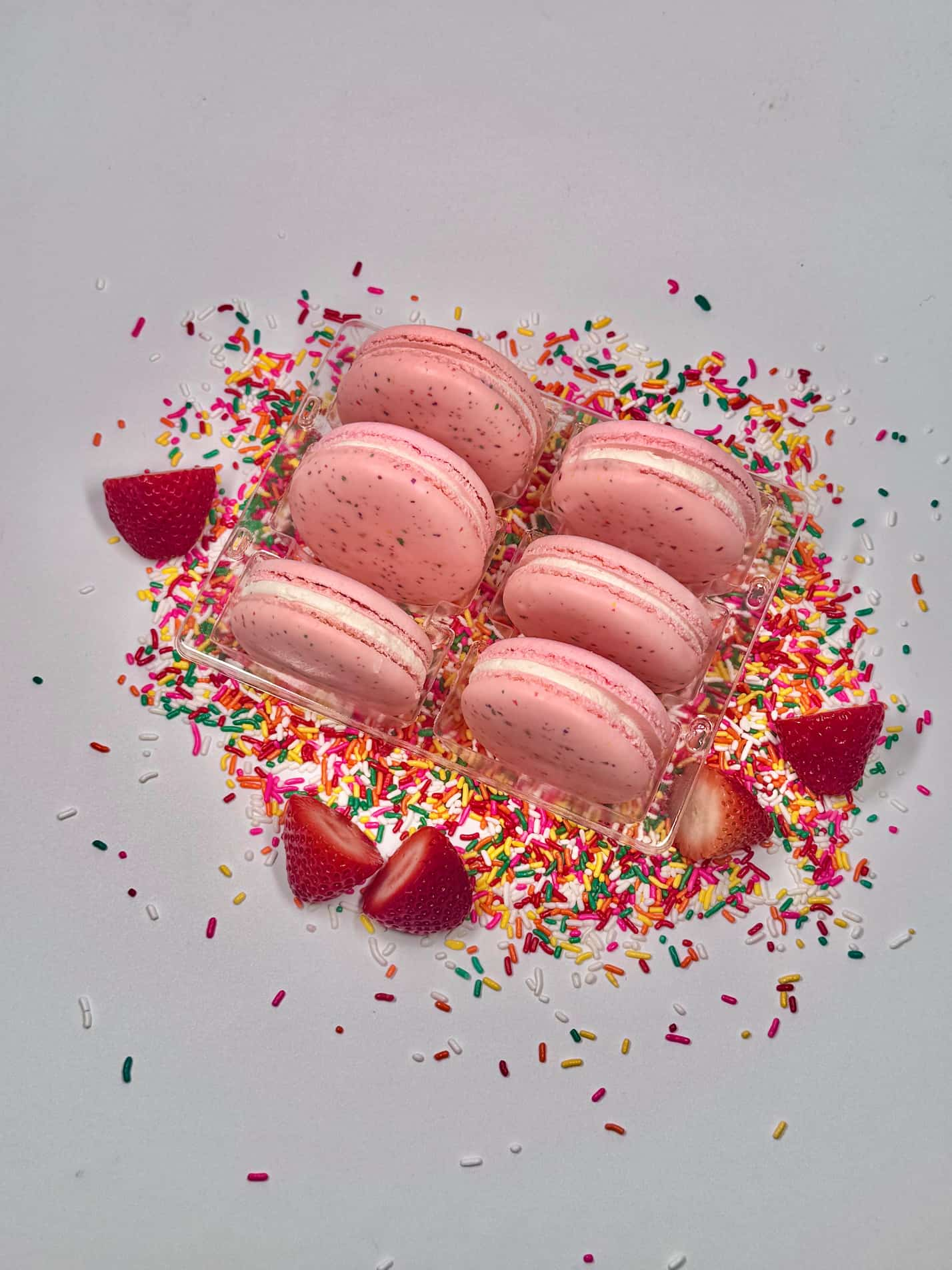 Strawberry Cupcake flavored french macarons on top of strawberries and rainbow sprinkles