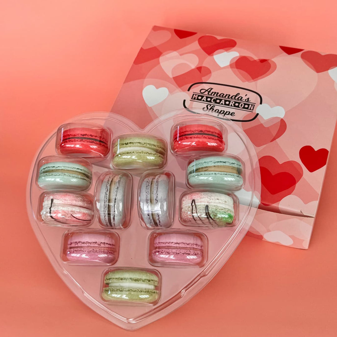 12 French macarons in a heart shaped pack sitting on top of a box with heart print