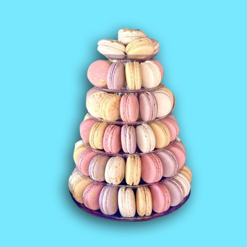 A six tier plastic tower filled with multicolored macarons against a blue background.